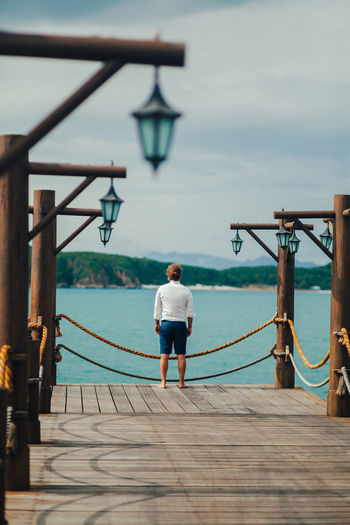 Rear view of man standing on pier over sea against sky
