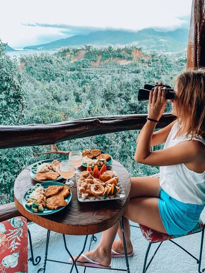 Woman using binoculars while sitting by food on table