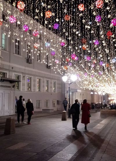People walking on illuminated christmas lights at night