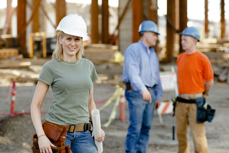 Portrait of female construction worker with two workers behind