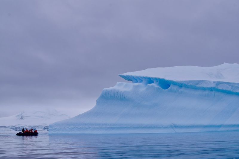 Group of adventures on a zodiac near a large iceberg in antarctica.