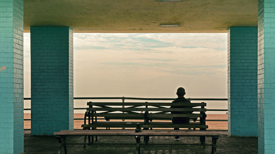 Rear view of man sitting on bench against sky