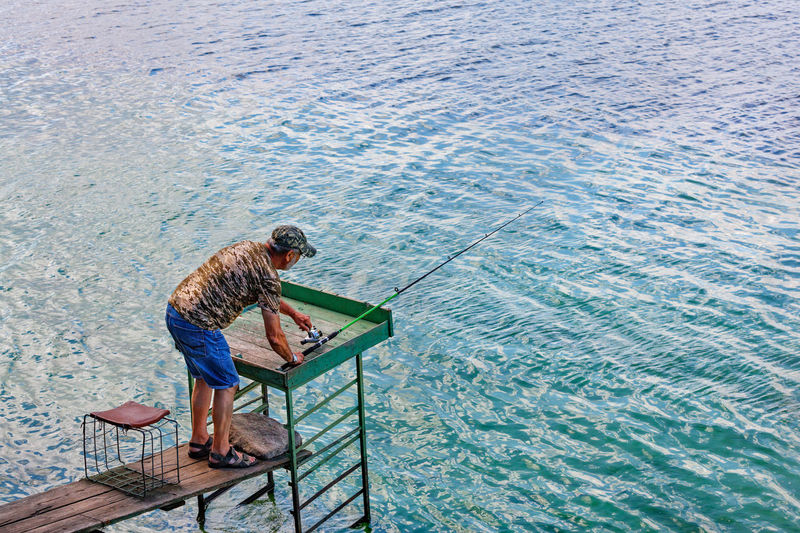 A fisherman is fishing by spinning on the river bank, standing on a wooden platform.