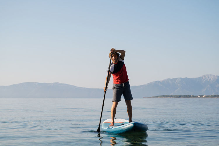 Full length of man paddleboarding in lake against sky