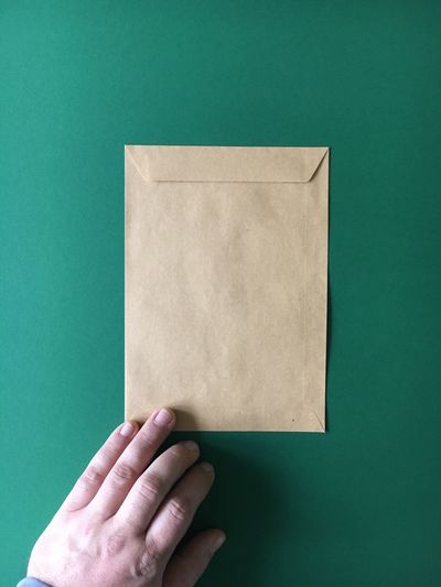 Cropped image of hand with envelop on green background