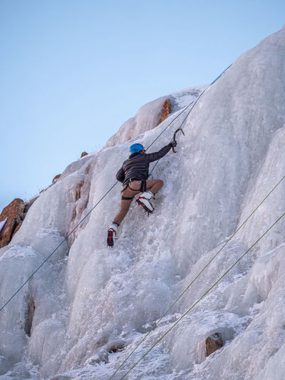 Low angle view of man ice climbing against clear sky