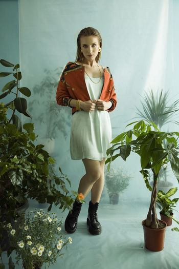 Full length of young woman standing against potted plants