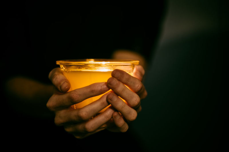 Midsection of person holding tea light candle in darkroom