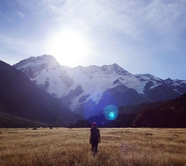 Rear view of woman walking against mountains at mt cook national park during sunny day