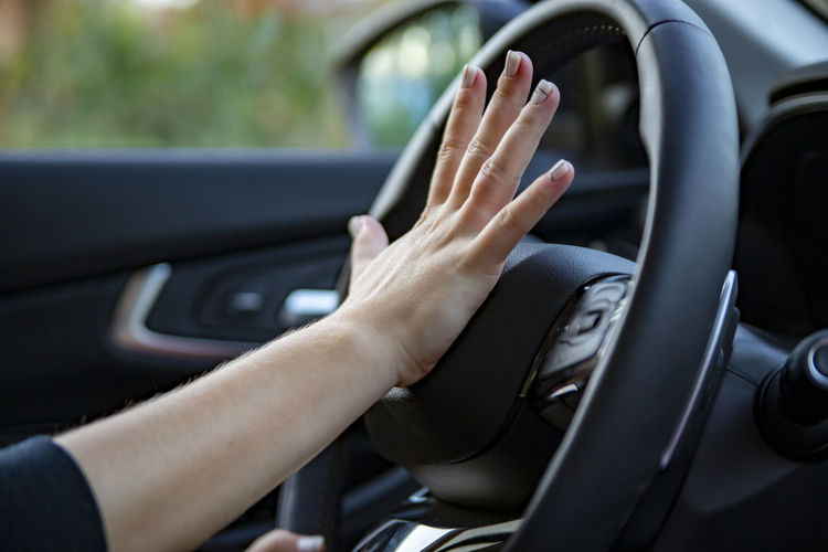 Hand presses the horn on the steering wheel of a modern car, no face person