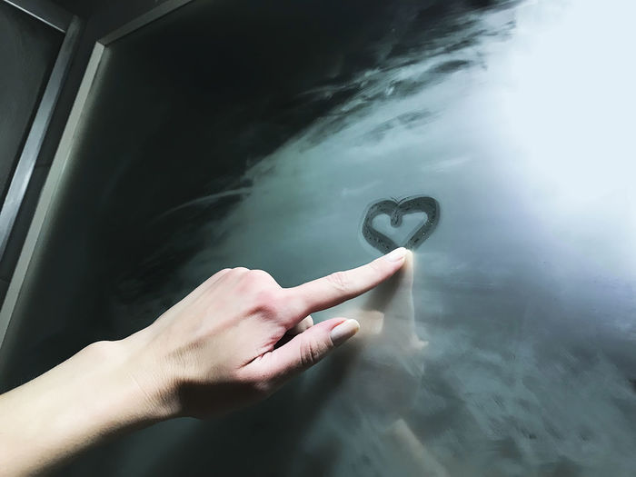 Cropped hand of woman drawing heart shape on wet mirror