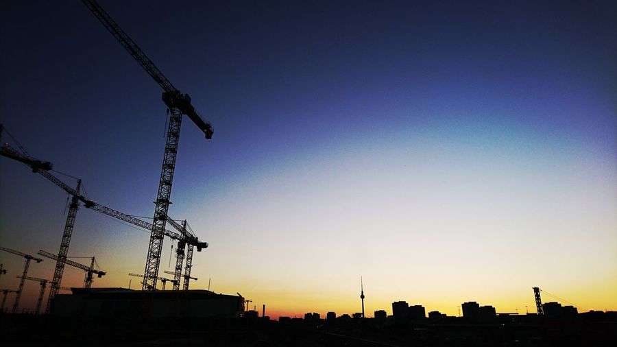 Low angle view of silhouette cranes against sky at dusk