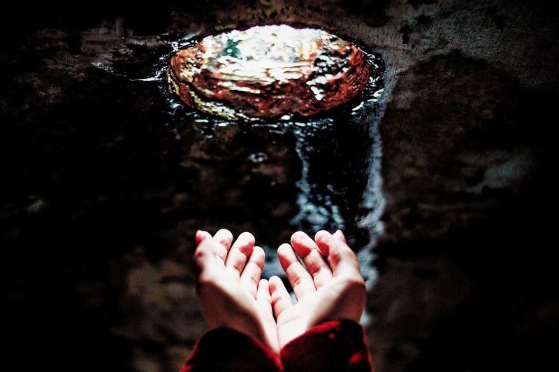 Cropped image of hands towards hole on wall with flowing water