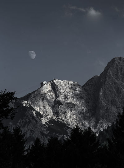 Low angle view of moon in mountains against sky