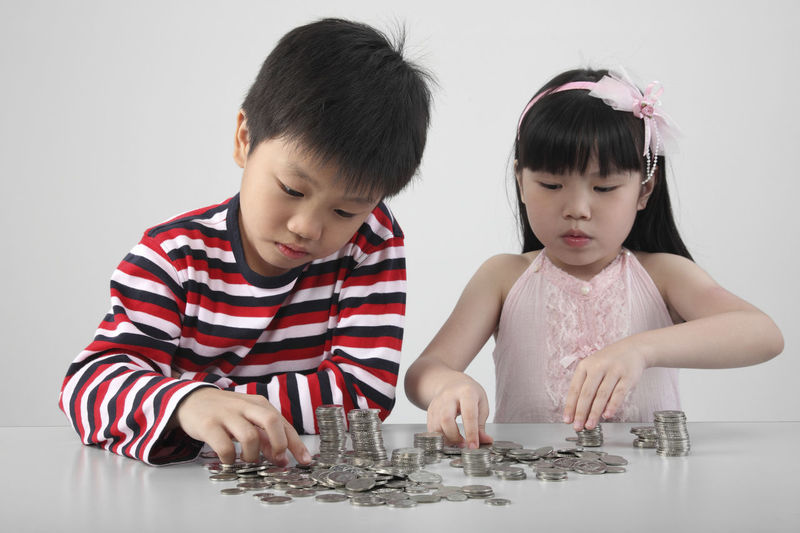 Children counting coins on table against white background