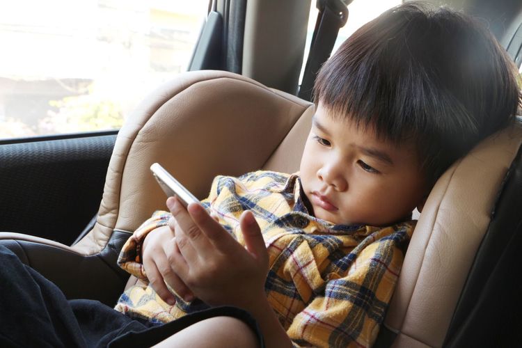 Asian boy looking at smartphone screen. child sitting on car seat and watch cartoon on mobile phone.