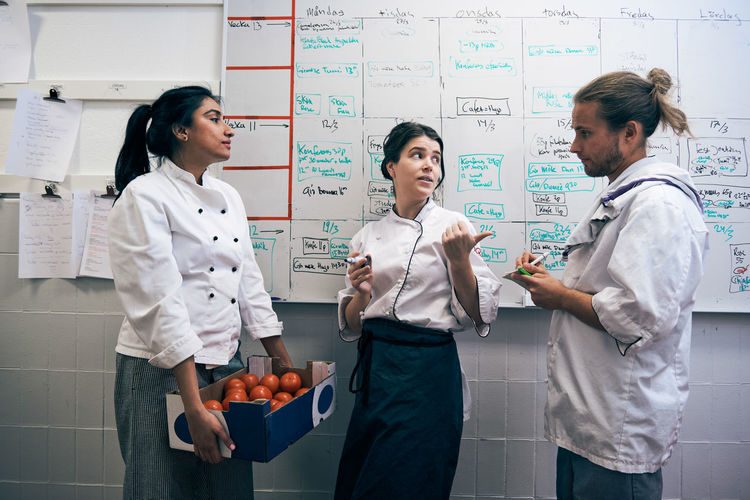 Chefs communicating against whiteboard in kitchen