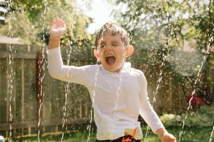 Young boy having fun with splashing water in backyard