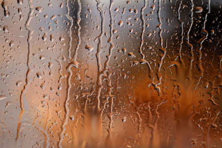 Full frame shot of wet glass and raindrops running down a window with a orange background