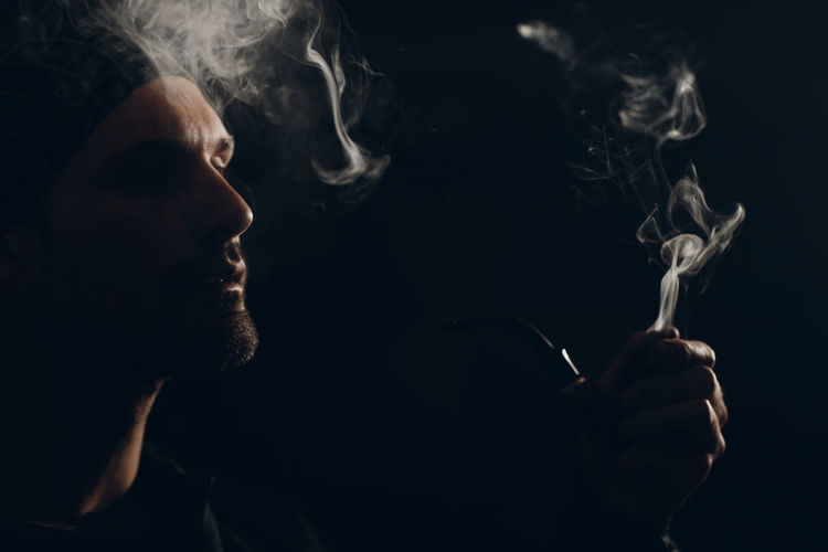 Man smoking pipe against black background
