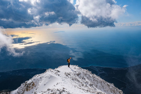 Man looking at sea by snowcapped mountain against sky