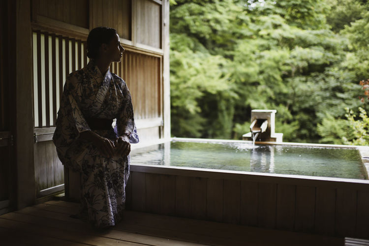 Young caucasian woman in a kimono getting ready to enjoy.a relaxing and traditional thermal waters bath at a japanese onsen, side view