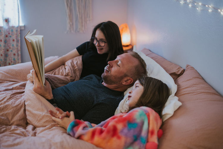 Horizontal image of family reading a book in bed
