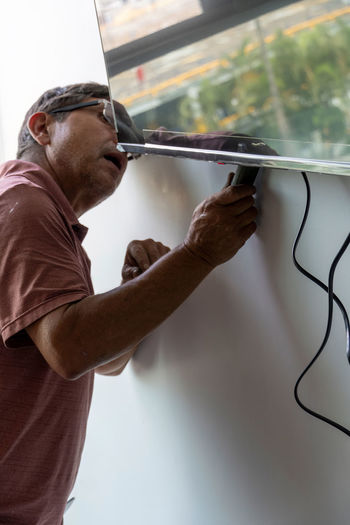 Latino man using a power drill to drill holes in the wall to hang a new television, drilling 