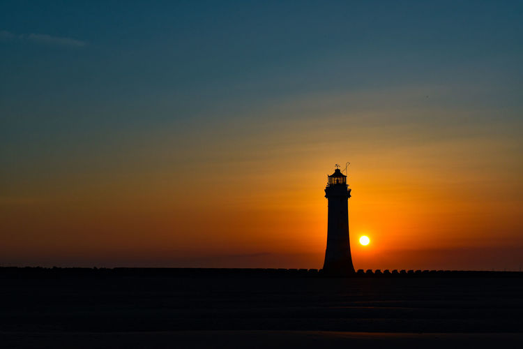 Silhouette lighthouse by sea against sky during sunset