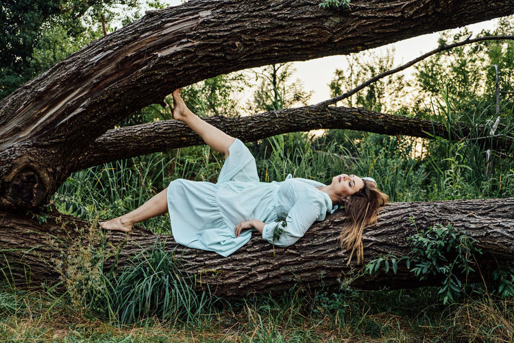 Peace of mind, breathing fresh air. alone woman in dress lying on tree