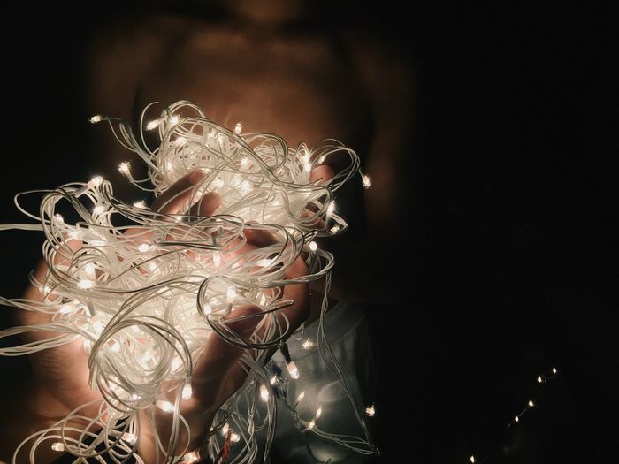 Cropped hands of man holding illuminated string lights by mirror in darkroom