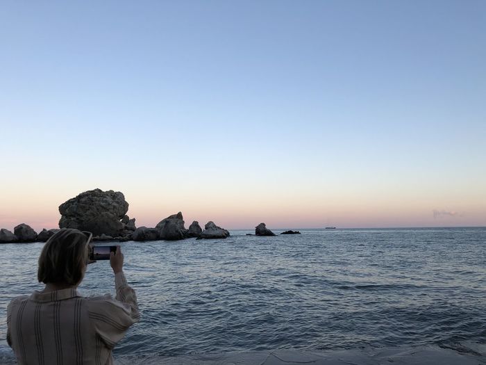 Rear view of woman photographing sea against clear sky