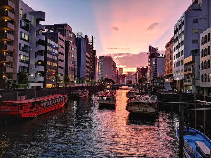 Boats moored in canal amidst buildings against sky during sunset