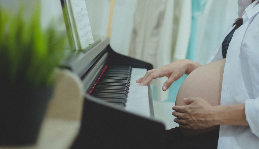 Midsection of pregnant woman playing piano at home
