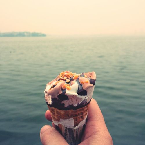 Cropped hand holding ice cream against sea