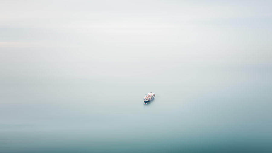 Small cargo container ship floating in middle sea and motion blur aerial view,