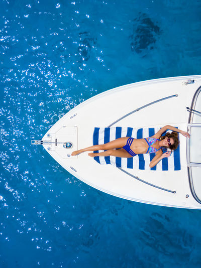 Directly above shot of woman lying in bikini on boat in sea