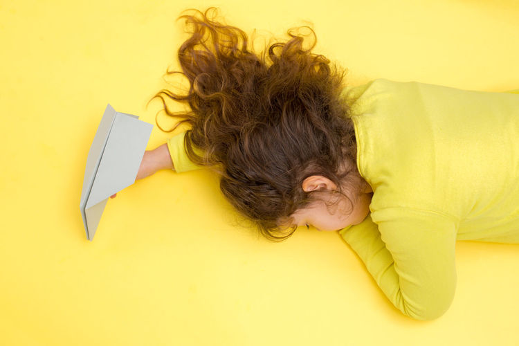High angle view of girl lying on yellow background