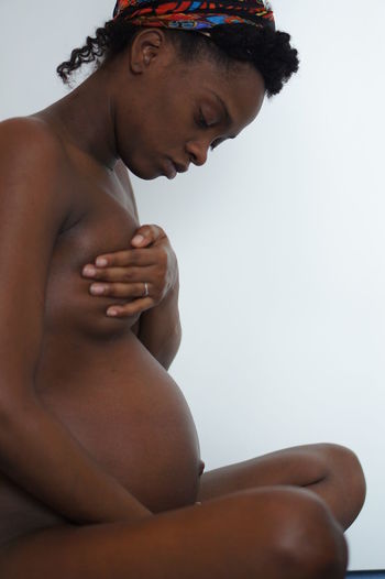 Side view of naked pregnant woman sitting against wall