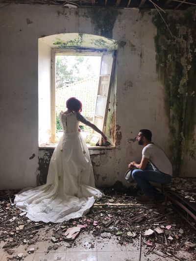 Bride standing by groom sitting in abandoned house 