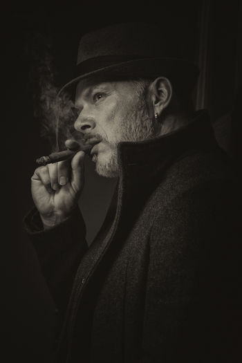 Portrait of man smoking cigar against black background