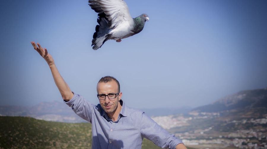 Portrait of man with pigeon flying against sky