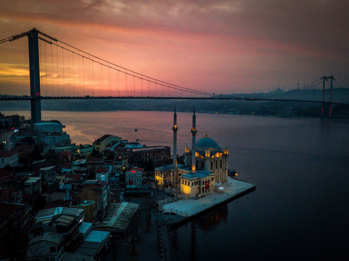 Suspension bridge over sea against sky during sunset and ortakoy mosque in foreground 