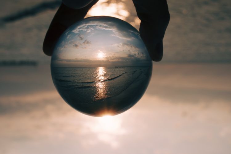 Midsection of person holding crystal ball against sky during sunrise 