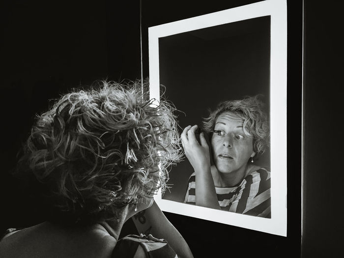 Reflection of woman in mirror while applying mascara
