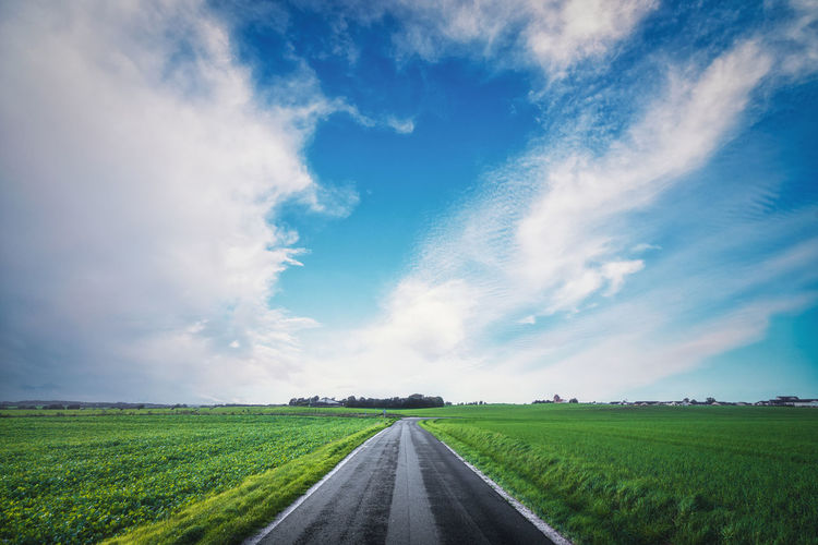 Asphalt road going through a rural landscape with green fields and a blue sky