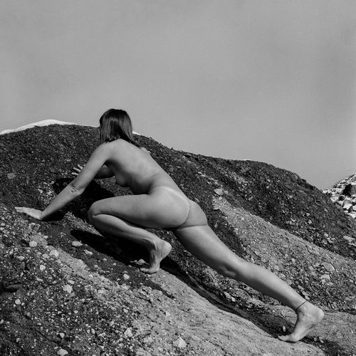 Naked woman crawling on rock against sky