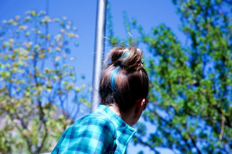 Low angle view of woman with dyed blue hair against trees on sunny day