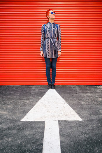 Full length of a woman standing at arrow against red shutter