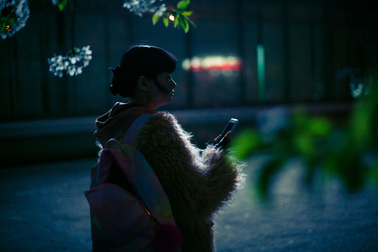 Woman holding phone while standing outdoors at night